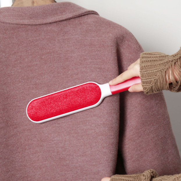 Person using a red and white brush on a brown sweater